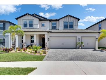 Beautiful two-story home boasts lush landscaping, a three-car garage, and a light gray brick paver driveway at 5026 Bromeliad Ave, Wimauma, FL 33598
