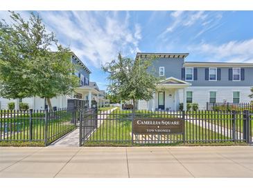 Camellia Square Townhomes with well-manicured lawns are framed by wrought iron fences and lush trees under a bright sky at 6619 S Manhattan Ave # 1, Tampa, FL 33616
