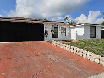 Charming single-story home with a black garage door and a red driveway under a partly cloudy sky at 7834 Treasure Pointe Dr, Port Richey, FL 34668