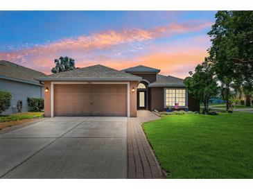 Charming single-story home featuring a well-manicured lawn, two car garage, and a beautiful sunset sky at 2708 Dolphin Watch Ct, Holiday, FL 34691