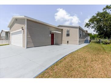 A charming home featuring tan siding, a garage, and a red front door with a freshly painted driveway at 8471 Fantasia Park Way, Riverview, FL 33578