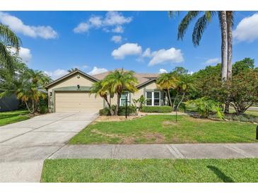 Charming single-story home featuring a manicured lawn, mature palm trees, and a two-car garage at 892 Crestridge Cir, Tarpon Springs, FL 34688