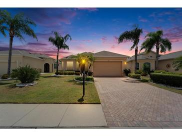 Charming single-story home featuring a brick driveway, lush landscaping, and beautiful palm trees at sunset at 1643 Emerald Dunes Dr, Sun City Center, FL 33573