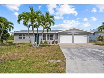 Charming single-story home featuring a two-car garage, tropical landscaping, and a bright blue front door at 4210 Palm Dr, Punta Gorda, FL 33950