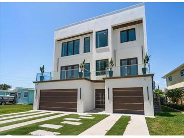 Striking modern home with a two-car garage, balcony, and manicured lawn at 16047 Redington Dr, Redington Beach, FL 33708