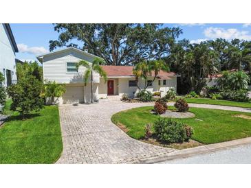 Charming home featuring a brick driveway, lush landscaping, and mature palm trees at 1238 Monterey Ne Blvd, St Petersburg, FL 33704