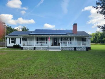 Inviting home with a charming front porch, solar panels, a brick chimney and a lush green lawn at 17430 Spring Valley Rd, Dade City, FL 33523