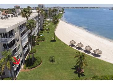 An aerial view of the condo building on the beach with green lawn, sand and beach umbrellas at 5701 Bahia Del Mar Cir # 108, St Petersburg, FL 33715