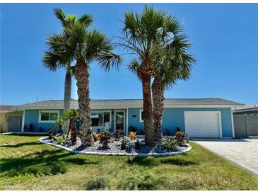 Charming home featuring light-blue siding, a well-manicured lawn, and beautiful landscaping with palm trees at 12300 4Th E St, Treasure Island, FL 33706