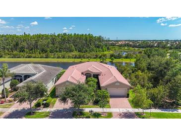 Charming single-story home features a red-tiled roof and lush landscaping, nestled next to a serene lake at 15860 Aurora Lake Cir, Wimauma, FL 33598