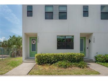 Modern townhome featuring a light-colored exterior, green door with floral wreath, and manicured landscaping at 1330 W Gray St # 1, Tampa, FL 33606