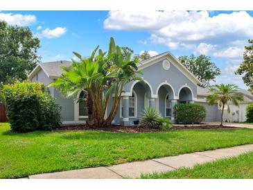 Charming single-story home featuring arched entrance, blue paint, lush landscaping, and a well-manicured lawn at 3703 Treeline Dr, Valrico, FL 33596