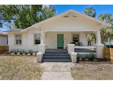 Charming bungalow featuring a teal front door, covered porch and well-maintained landscaping at 1003 E Emma St, Tampa, FL 33603