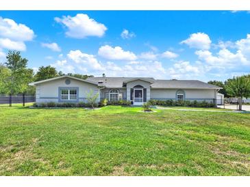 Inviting one-story home with a lush green lawn, mature landscaping, and a screened front entrance at 6219 Wendell Dr, Wesley Chapel, FL 33544