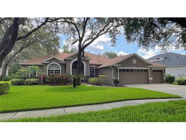 Charming one-story home featuring a manicured lawn, mature trees, and a welcoming three-car garage at 5704 Eaglemount Cir, Lithia, FL 33547