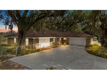 Beautiful exterior of a brick home featuring a manicured lawn and a long driveway leading to an attached garage at 9542 Wallien Dr, Brooksville, FL 34601