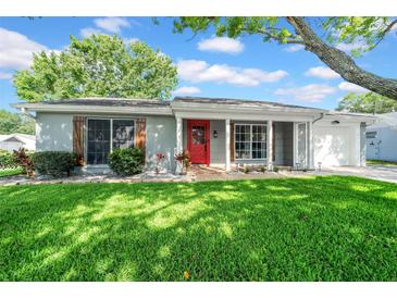 Charming single-story home featuring a well-manicured lawn, a bright red front door, and tasteful landscaping at 12401 Yorktown Ln, Bayonet Point, FL 34667