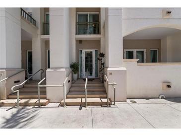 Inviting building entrance featuring bright stucco, steps, and minimalist hand railings leading to a glass door at 450 Knights Run Ave # 104, Tampa, FL 33602