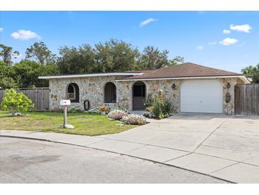 Charming stone-clad home featuring a well-manicured lawn, flower beds and an attached one car garage at 8918 Carmen Ln, Port Richey, FL 34668