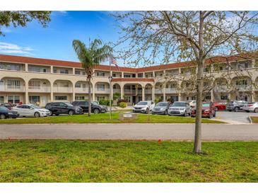 Three-story condo complex featuring parking, palm trees, and manicured landscaping under a blue sky at 2434 Australia E Way # 38, Clearwater, FL 33763
