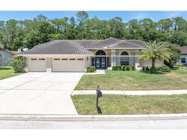 Charming home featuring a three-car garage, tile roof, lush lawn, and meticulously manicured landscaping at 4049 Wellington Pkwy, Palm Harbor, FL 34685