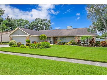 Charming single-story home features beautiful landscaping, a well-maintained lawn, and stone accents at 13810 Lake Village Pl, Tampa, FL 33618