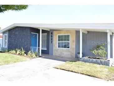Charming single-story home featuring a textured exterior, landscaped yard, and a bright blue front door at 6527 S West Shore Cir, Tampa, FL 33616