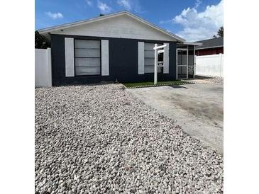 View of single-story home with dark siding, white trim, stone ground cover, and 'For Sale' sign at 9106 Telford Ct, Tampa, FL 33615