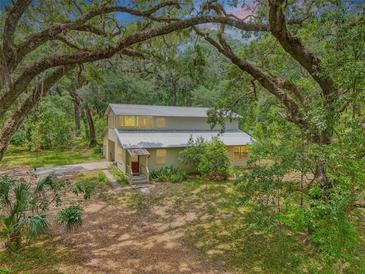 Secluded two-story home with a metal roof nestled among mature trees and a lush landscape at 7189 Griffin Rd, Brooksville, FL 34601