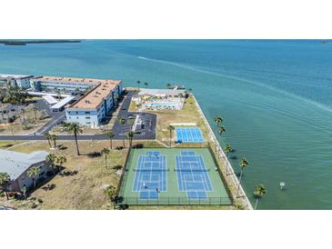Aerial view featuring tennis courts, shuffleboard courts, a community pool, and water views at 7 Elgin Pl # 202, Dunedin, FL 34698