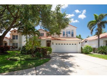 Charming two-story home with terra cotta roof, a manicured lawn, mature trees, and a white, six-panel garage door at 2969 La Concha Dr, Clearwater, FL 33762