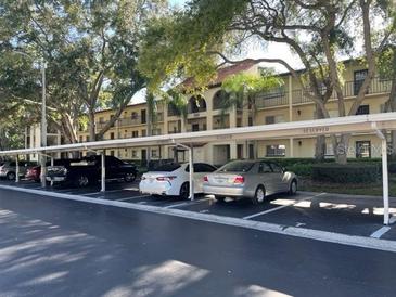 Exterior view of a condominium complex showing parking spaces, trees and landscaping on a sunny day at 3077 Casa Del Sol Cir # 207, Clearwater, FL 33761