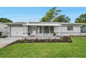 Charming home featuring a cozy front porch, well-maintained lawn, and beautiful landscaping at 3100 70Th N St, St Petersburg, FL 33710