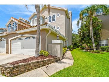 Beautiful multi-story home featuring manicured lawn, an attached garage, and tropical landscaping at 1676 Arabian Ln, Palm Harbor, FL 34685
