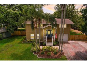 Charming two-story home featuring a landscaped front yard with palm trees and an American flag at 611 Shore E Dr, Oldsmar, FL 34677
