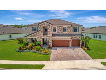 Beautiful two-story home with stone accents, three-car garage, manicured lawn, and colorful landscaping at 9136 Warm Springs Cir, Parrish, FL 34219