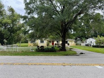 Charming single-story home with a well-manicured lawn, red door, and mature trees at 15034 Lake Magdalene Blvd, Tampa, FL 33618