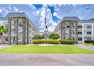 Low angle view of a condo building with green grass, well maintained landscaping, and an American flag in front of the building at 4801 Airport Rd # 211, Zephyrhills, FL 33542