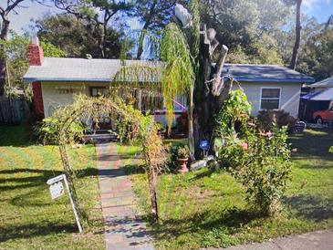 Charming one-story home featuring a manicured lawn, brick chimney and a pathway leading through a floral archway at 7195 65Th N St, Pinellas Park, FL 33781