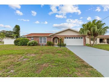 Charming brick home with a well-maintained lawn, arched entryway, and two-car garage, under a partly cloudy, blue sky at 326 Circle Dr, Palm Harbor, FL 34683