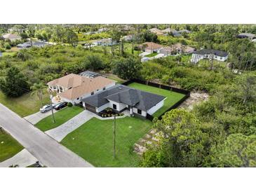Beautiful aerial view of the house, showcasing its dark roof, green lawn, and proximity to lush greenery at 14009 Wenzel Ave, Port Charlotte, FL 33981