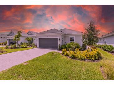 Charming single-story home featuring manicured landscaping, a gray two-car garage door, and a paver driveway at 16126 San Donato Pl, Bradenton, FL 34211