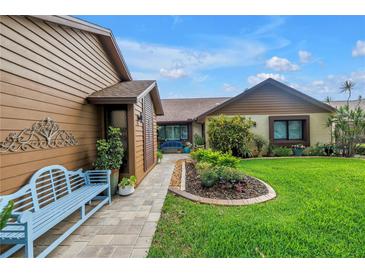 Charming home featuring a well-manicured lawn, lush landscaping, and inviting entryway with a comfortable, light blue bench at 2475 Bay Berry Dr, Clearwater, FL 33763