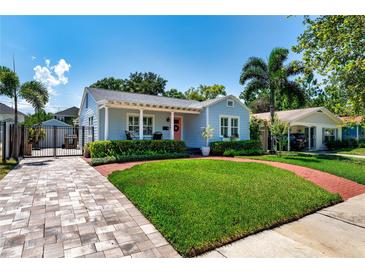 Charming blue home boasts lush landscaping, a brick walkway, and an inviting front porch with seating at 115 S Beverly Ave, Tampa, FL 33609