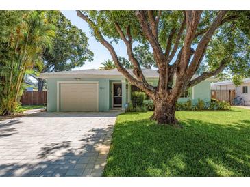 Charming single-story home featuring a well-manicured lawn, paver driveway, and a large shade tree at 1281 Robin Hood Ln, Dunedin, FL 34698