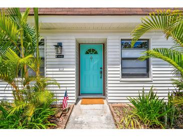 Charming white home exterior features a vibrant turquoise front door surrounded by lush, tropical landscaping at 9142 Oakwood Ln, Seminole, FL 33776