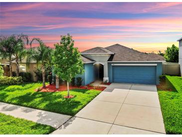 Charming single-story home with a well-maintained lawn, mature trees, and attached two-car garage under a colorful sky at 17136 Sunshine Mimosa: St, Wimauma, FL 33598