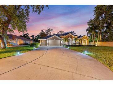 Beautiful home with a long driveway and lush landscaping, illuminated by landscape lighting at twilight at 512 Creekside Ct, Safety Harbor, FL 34695