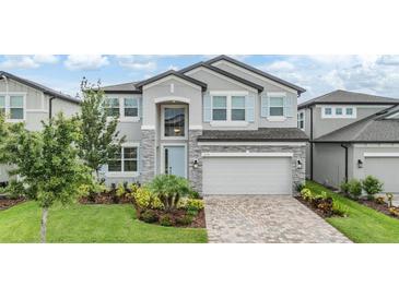 Two-story home with stone accents, a manicured lawn, paver driveway, and light blue shutters at 7276 Notched Pine Bnd, Wesley Chapel, FL 33545