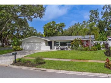 Charming single-story home featuring a lush green lawn and mature trees, with a brick-paved driveway at 1368 Whispering Pines Dr, Clearwater, FL 33764